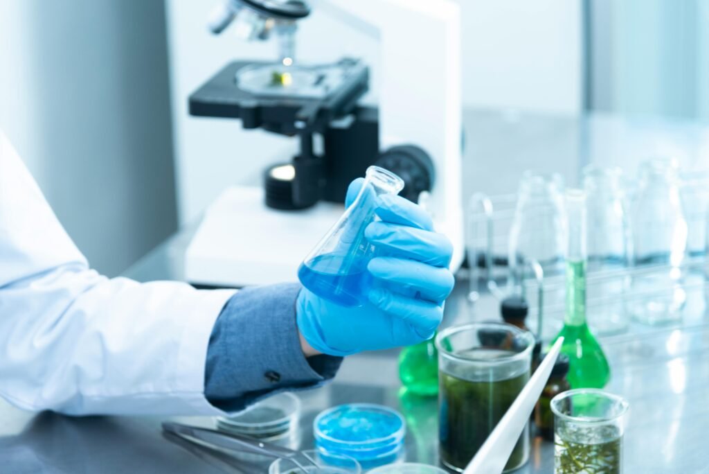 pexels-photo-2280571-2280571 Scientist in gloves analyzing blue liquid in a laboratory setting with microscope and glassware.
